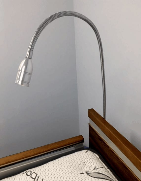 A flexible, metallic ImpulseEssence39 gooseneck lamp is attached to the edge of a wooden surface and extends upward and outward.