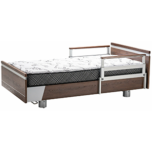 A hospital-style single bed, Apr2025 ImpulseEssence36, with a sturdy wooden frame, adjustable metal side rails, and a patterned mattress.