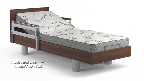 A wooden-frame adjustable bed with a patterned mattress and metal assist rails on the side. Text reads: "Impulse Bed shown with optional Assist Rails.